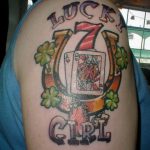 Фото тату на плече с изображением семерки, карты, клевера и надписи 'LUCKY GIRL' в ярких цветах.