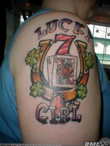 Фото тату на плече с изображением семерки, карты, клевера и надписи 'LUCKY GIRL' в ярких цветах.