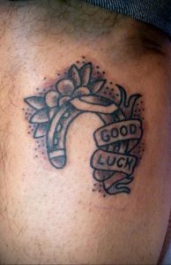 Фото минималистичной татуировки подковы с надписью "Good Luck". Небольшой черно-белый рисунок татуировки на руке.
