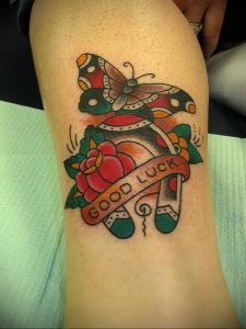 Фото тату бабочки и подковы с надписью 'GOOD LUCK' в стиле олд скул. Яркие цвета, четкие контуры, татуировка на руке.
