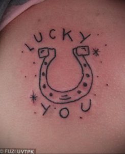 Фото простой татуировки подковы с надписью 'LUCKY YOU'. Минималистичный дизайн, контурный рисунок, татуировка на плече.