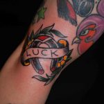 Фото тату подковы с надписью 'LUCK' в стиле олд скул на руке. Красочные цвета, традиционный дизайн, четкие контуры.