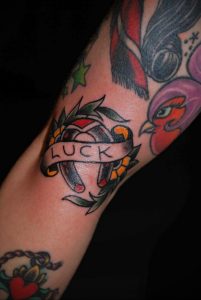 Фото тату подковы с надписью 'LUCK' в стиле олд скул на руке. Красочные цвета, традиционный дизайн, четкие контуры.