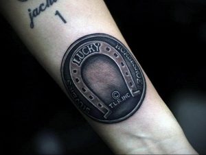 Фото тату подковы в стиле black and grey на предплечье. Реалистичный рисунок, детализированная проработка, эффект металла.