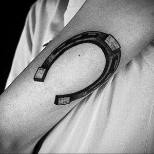 Фото тату подковы в стиле blackwork на предплечье. Черно-белый рисунок, четкие линии, минималистичный дизайн.