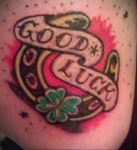 Фото тату в стиле олд скул с изображением подковы, клевера и надписи 'Good Luck' на руке.