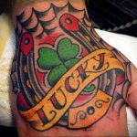 Фото тату на руке с изображением зеленого клевера, подковы и надписи 'Lucky' в традиционном стиле.