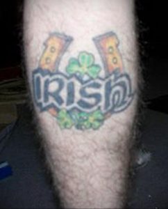 Фото тату на икре: надпись 'IRISH' с четырехлистным клевером и подковами, выполненное в традиционном стиле.