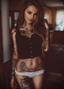 Фотография девушки с множеством темных татуировок на руках, груди и животе, одетой в черное.