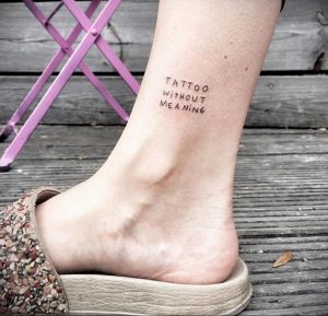 Фото минималистичной татуировки на лодыжке с надписью 'Tattoo Without Meaning' черными чернилами. Изящный шрифт и небольшие размеры делают ее стильной.