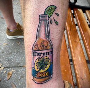 Фото татуировки с изображением бутылки пива Corona, украшенной черепом, клевером и цифрой 2020. Оригинальный рисунок, сочетающий символы удачи и опасности.