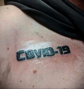Фото тату с объемной надписью 'COVID-19' на шее. Татуировка выполнена в черном цвете с использованием теней.