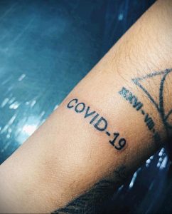 Фото тату с надписью 'COVID-19' на предплечье. Простая и лаконичная татуировка черного цвета.