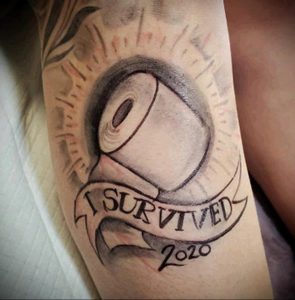 Черно-серая татуировка с изображением вируса COVID-19 и надписью "I survived 2020", символизирующая пережитый год пандемии.