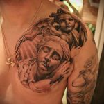 Фото тату на плече и груди: реалистичный ангел, склонившийся над розой, выполненный в черно-серых тонах. Детализированный рисунок татуировки с мягкими переходами и тенями.