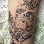 Фото тату совы в короне на руке. Детализированный рисунок с голубыми глазами и реалистичными перьями. Идеальный эскиз для любителей птиц.