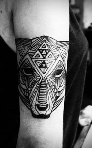 Фото тату на руке, изображающее стилизованную голову волка, выполненную в геометрическом стиле с использованием черных линий.