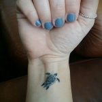 Фото тату маленькой черепашки на запястье. Черно-белый рисунок в стиле минимализм, выполненный тонкими линиями.