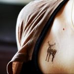 Фото тату маленького оленя с рогами, выполненного в технике лайнуорк на ключице девушки. Изящный рисунок татуировки.