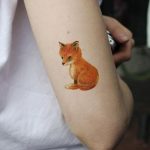 Фото тату лисенка на руке. Детализированный рисунок в теплых тонах, имитирующий акварельную живопись, символизирующий хитрость и ум.