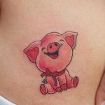 Фото тату поросенка с красным бантиком на животе. Нежный и игривый рисунок, выполненный в ярких цветах, для любителей животных.