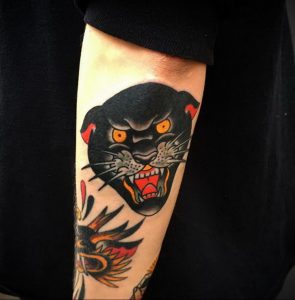 Фото тату пантеры на руке в стиле олд скул. Выражение ярости на морде, яркие цвета, четкие контуры и детализированные клыки.