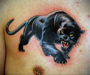 Фото тату: черная пантера в прыжке на груди. Детализированный рисунок татуировки с желтыми глазами и острыми когтями.