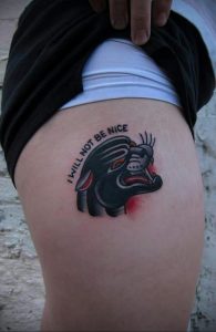 Фото тату: маленькая черная пантера с надписью "I WILL NOT BE NICE" на бедре, выполненная в стиле олд скул.