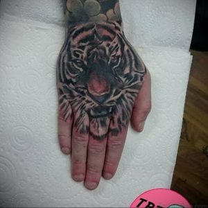 Фото тату: Реалистичная татуировка головы тигра на ладони. Детализированная проработка шерсти и глаз создает впечатляющий эффект.
