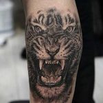 Фото тату: Реалистичный рычащий тигр на голени, выполненный в черно-серых тонах. Детализированный рисунок татуировки.