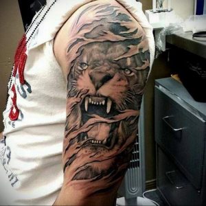 Фото татуировки тигра на плече, выполненной в стиле blackwork. Использование только черного цвета создает эффектный и контрастный рисунок.
