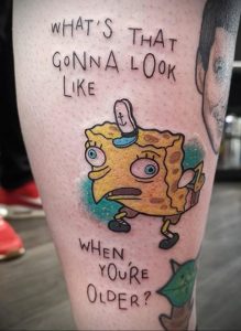Фото тату: яркая и юмористическая татуировка Спанч Боба с надписью 'What's that gonna look like when you're older?' на руке.