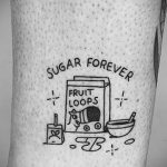Фото тату: красочная татуировка с изображением коробки хлопьев 'Fruit Loops' и чашки с хлопьями на руке. Рисунок татуировки выполнен в мультяшном стиле.