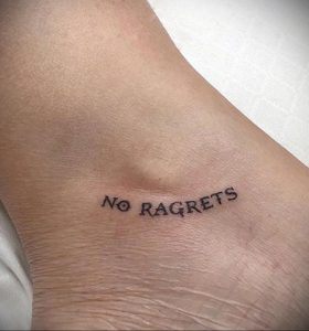 Фото тату: небольшая татуировка надписью 'No Regrets' на лодыжке. Простой и лаконичный рисунок татуировки, выполненный черным цветом.