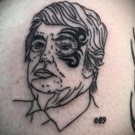 Фото тату на руке с изображением портрета человека в стилизованной манере. Черно-белый рисунок с четкими линиями.