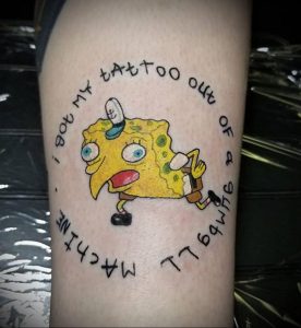 Фото тату с изображением Губки Боба в круге с надписью 'I GOT MY TATTOO OUT OF A MACHINE'. Веселый и яркий рисунок на руке.