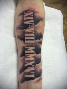 Фото тату: На предплечье изображены римские цифры 'XIV-VIII-MMXVI' в сочетании с акварельными брызгами черного и серого цветов.
