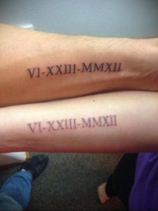 Фото тату: парные татуировки с черными римскими цифрами 'VI-XXIII-MMXII' на предплечьях двух людей, символизирующие общую дату и связь.