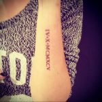 Фото татуировки на предплечье с римскими цифрами IV X MCMXCV. Черный цвет, четкие линии, минималистичный стиль. Идеально для тех, кто ценит лаконичность.