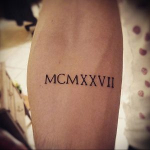 Фото татуировки на руке с римскими цифрами MCMXXVII. Черный цвет, четкие линии, классический стиль. Идеально для тех, кто ценит лаконичность.