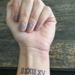 Фото татуировки на запястье с римскими цифрами, выполненными черным цветом. Минималистичный дизайн, четкие линии.