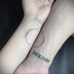 Фото парных татуировок с географическими координатами и римскими цифрами на запястьях. Черный рисунок татуировки, минималистичный стиль, символизирует место и дату.