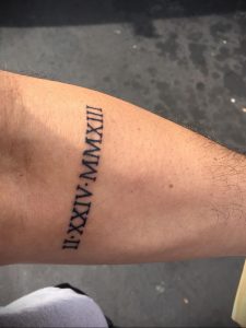 Фото татуировки на руке с римскими цифрами 'II.XXIV.MMXIII'. Черный цвет, четкие линии, минималистичный дизайн.