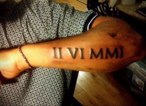 Фото тату: татуировка римскими цифрами 'II VI MMI' на запястье. Черный цвет, четкие линии, минималистичный дизайн.