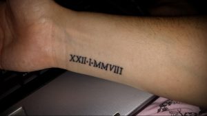 Фото тату: татуировка римскими цифрами 'XXII-I-MMVIII' на запястье. Черный цвет, четкие линии, минималистичный дизайн.