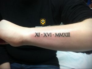 Фото тату: татуировка римскими цифрами 'XI XVI MMXIII' на предплечье. Черный цвет, четкие линии, минималистичный дизайн.