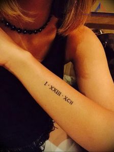 Фотография татуировки на предплечье с римскими цифрами 'I.XXIII.XCII'. Черный цвет, тонкие линии, изящный дизайн.