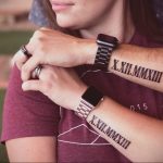 Фотография парных татуировок на предплечьях, изображающих римские цифры 'X.XII.MMXIII'. Черный цвет, четкие линии, символизирующие связь между двумя людьми.