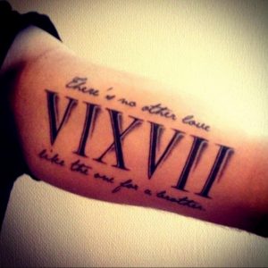 Фотография татуировки на предплечье с римскими цифрами 'VI.XVII' и надписью 'There's no other love like the one for a brother'. Черный цвет, стилизованный шрифт.