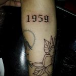 Фото тату: татуировка с годом '1959' в готическом стиле на мужском предплечье. Черный цвет, острые углы, выразительный дизайн.